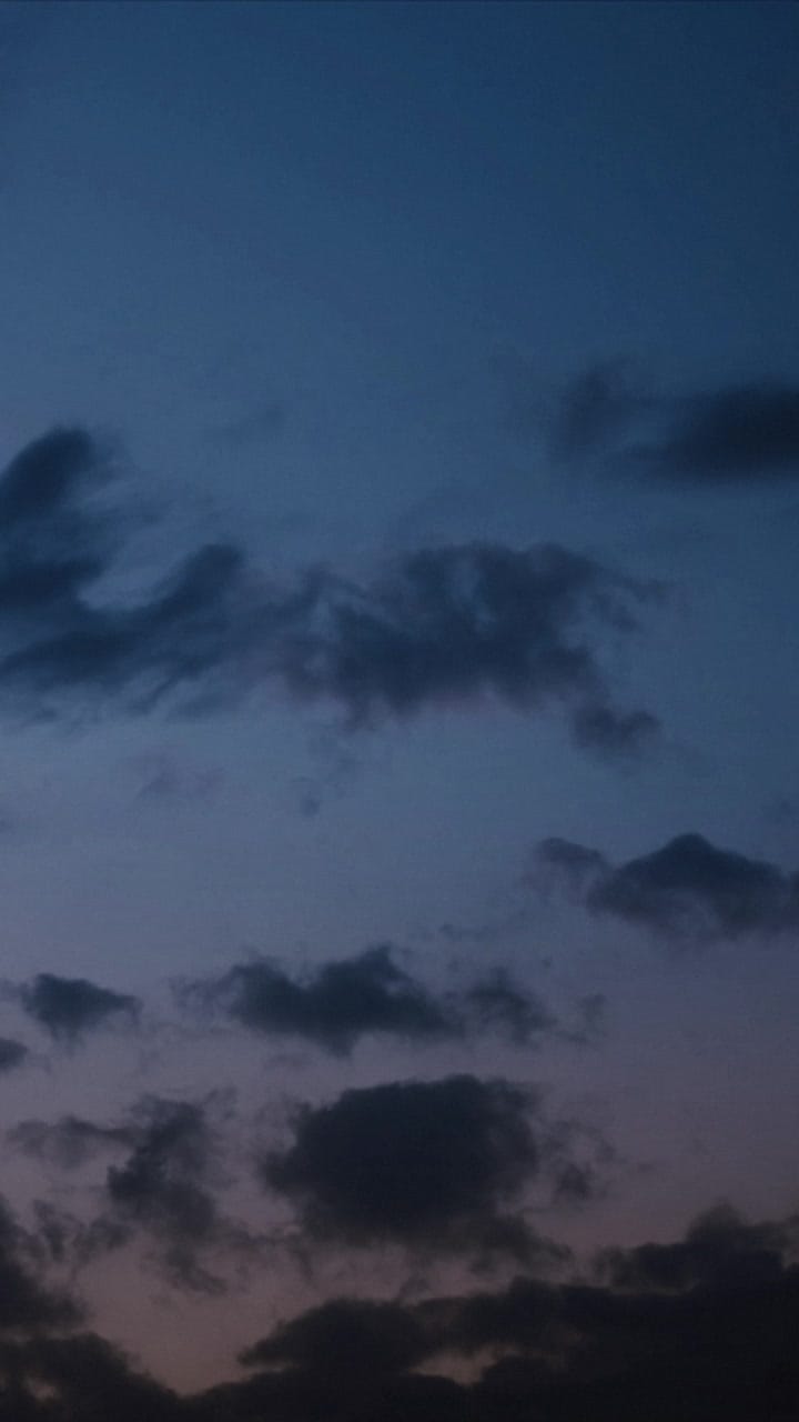 Céu da hora azul com nuvens passando devagar e uma faixa de luz no horizonte, a noite chegando.